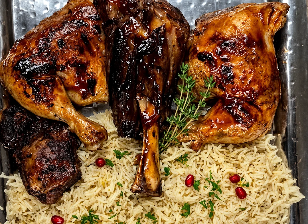 Smoked lamb shank and BBQ chicken quarters over rice on a steel tray