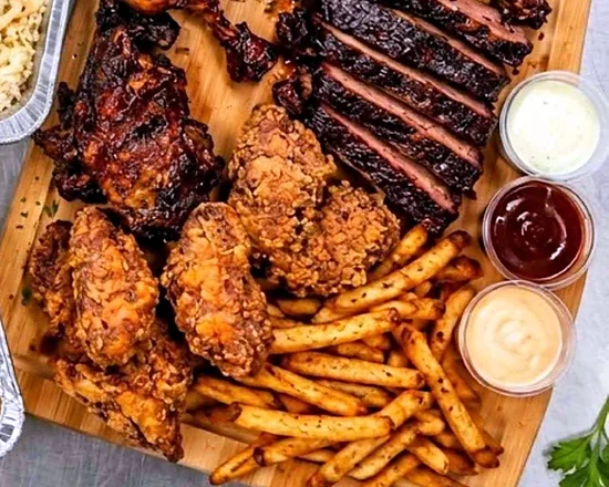 Platter for 2 with sliced smoked beef, fried chicken, fries and dipping sauces on a BBQ board